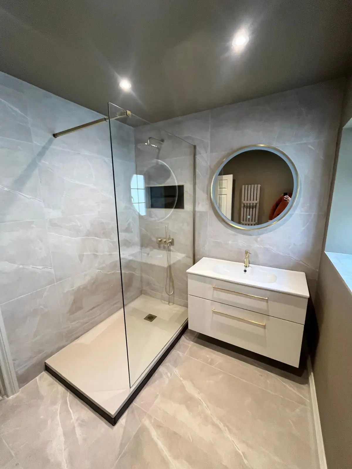 The same bathroom after refurbishment, with a walk-in shower, round mirror and vanity unit