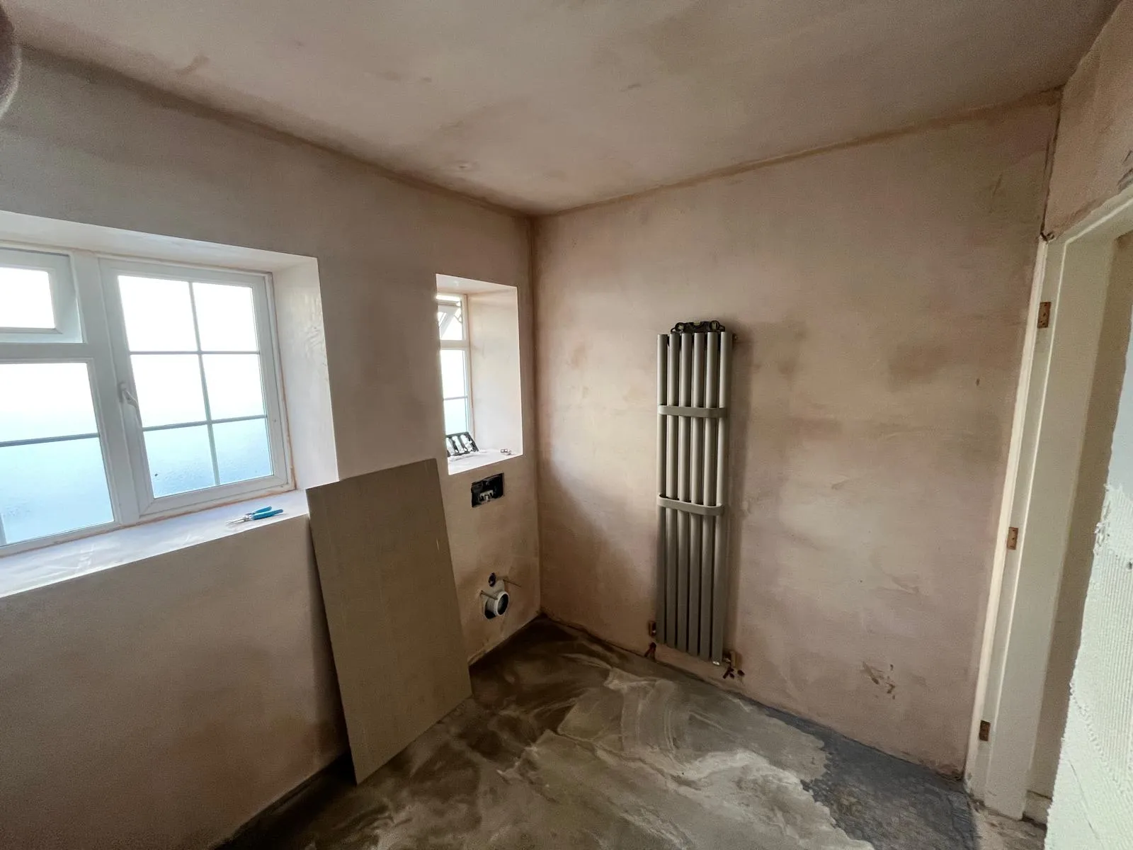 Freshly plastered bathroom walls with a vertical radiator