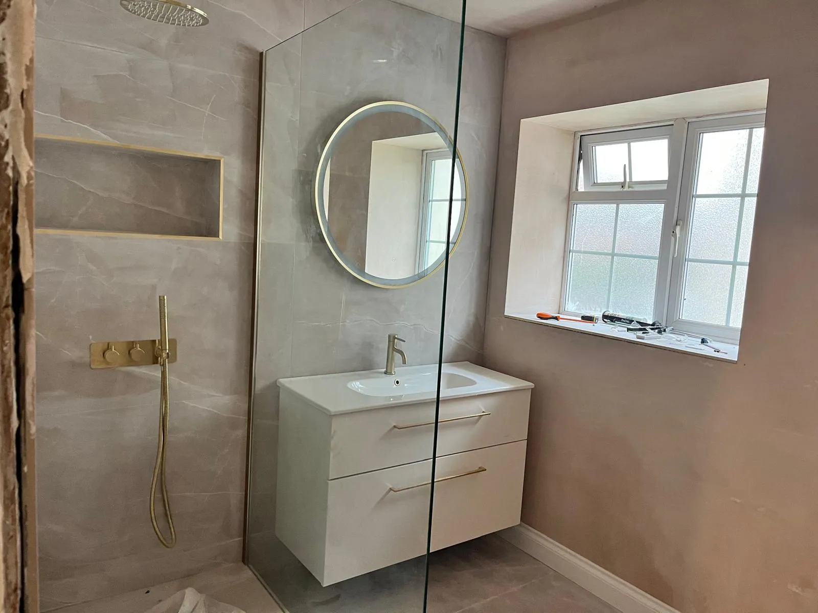 Tiled shower area with a recessed niche, round mirror and vanity unit