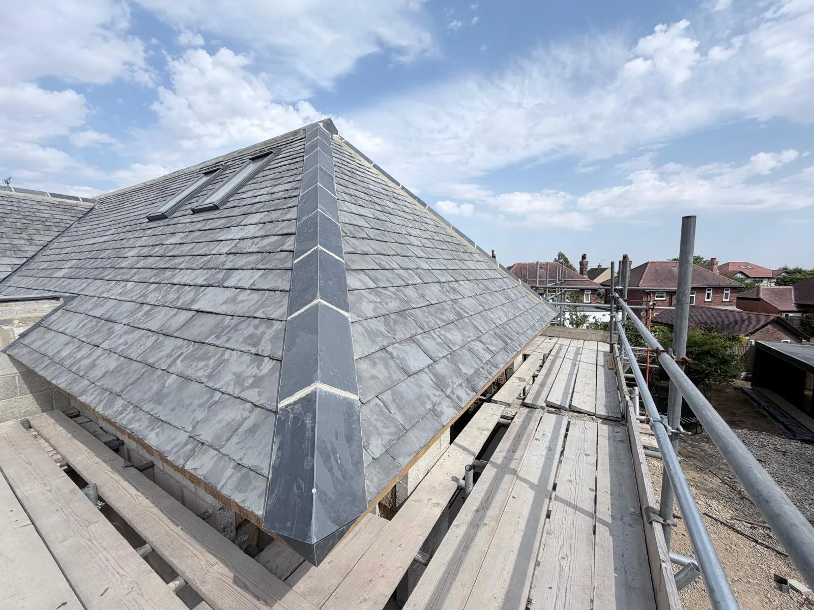 Completed slate hip roof with rooflights under a blue sky