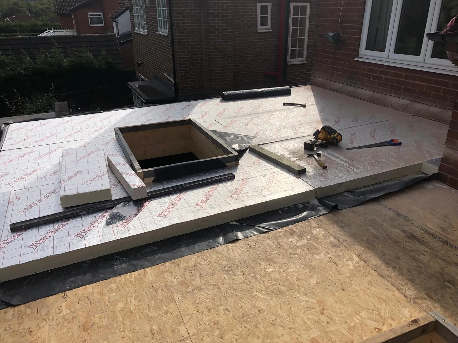 Insulation boards laid on a flat roof deck around a timber rooflight upstand