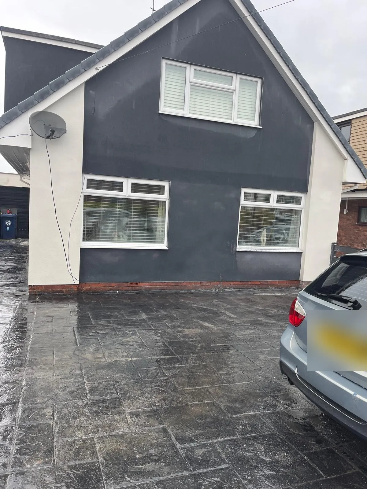 Front of a house finished in dark grey render with white window surrounds