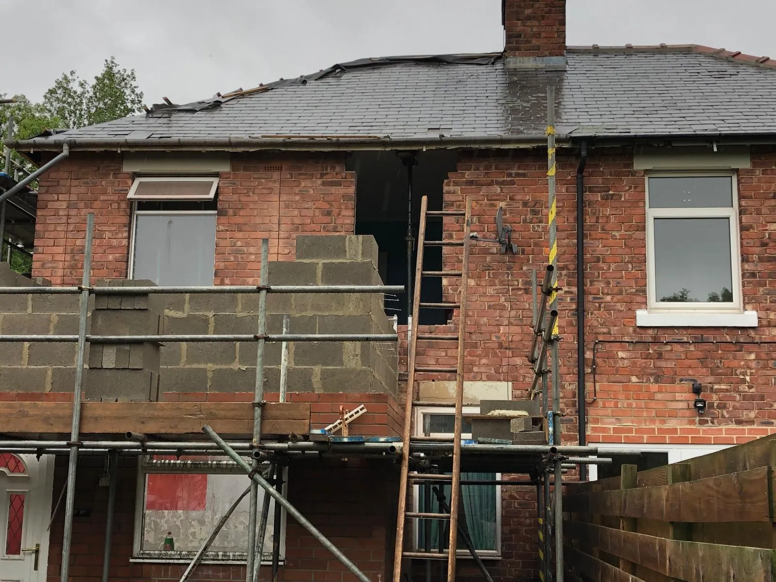 Scaffold around new blockwork walls rising at first-floor level on the back of a red-brick house