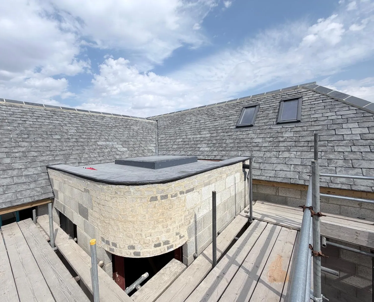 New slate roof with rooflights beside a stone-faced bay, seen from the scaffold